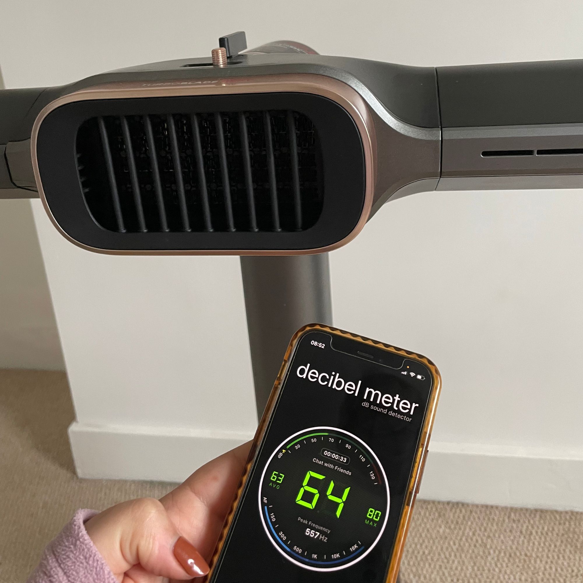 Hand holding a phone with a decibel meter app on it, in front of the Shark TurboBlade Cool + Heat TH200UK