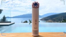 The Dyson HushJet Mini Cool Fan sat on a table in front of a pool with picture corners around it