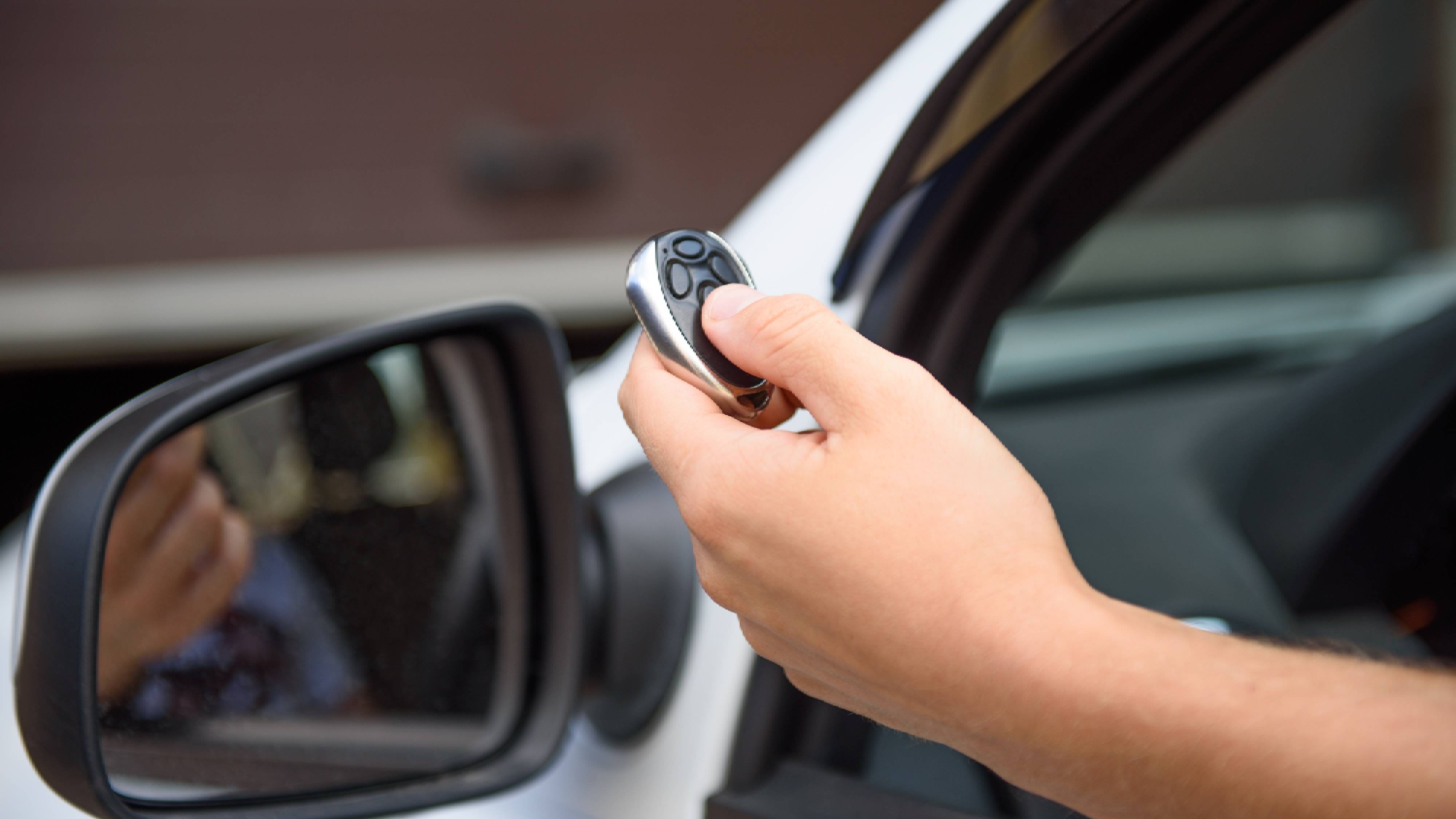 Close-up of a hand pressing a multi-button garage remote next to a car window