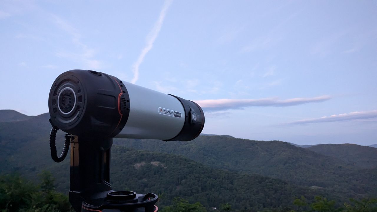 a black and white telescope in a field with trees behind it