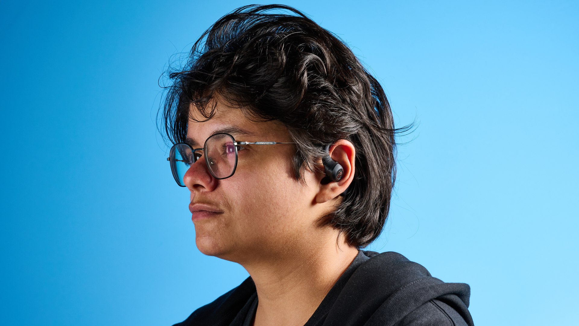 Jlab epic open sport open-earbuds in a black colorway photographed on a blue background.