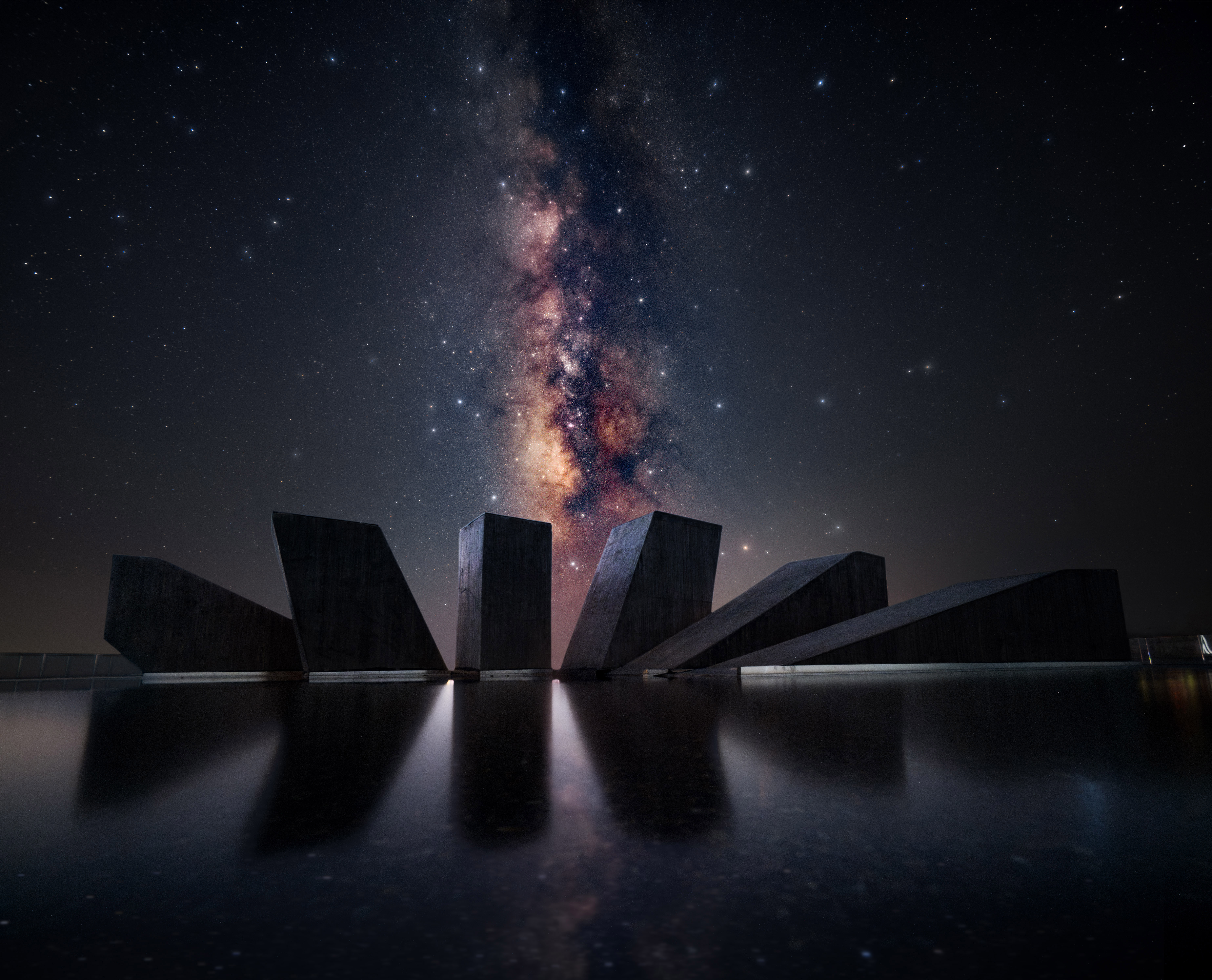 A photo of the Milky Way galaxy behind a man made sculpture on still water
