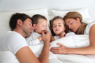 Children snuggle in bed with their parents.