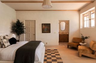 A bedroom with wooden floors, white bedding, low chairs and a minimalist light