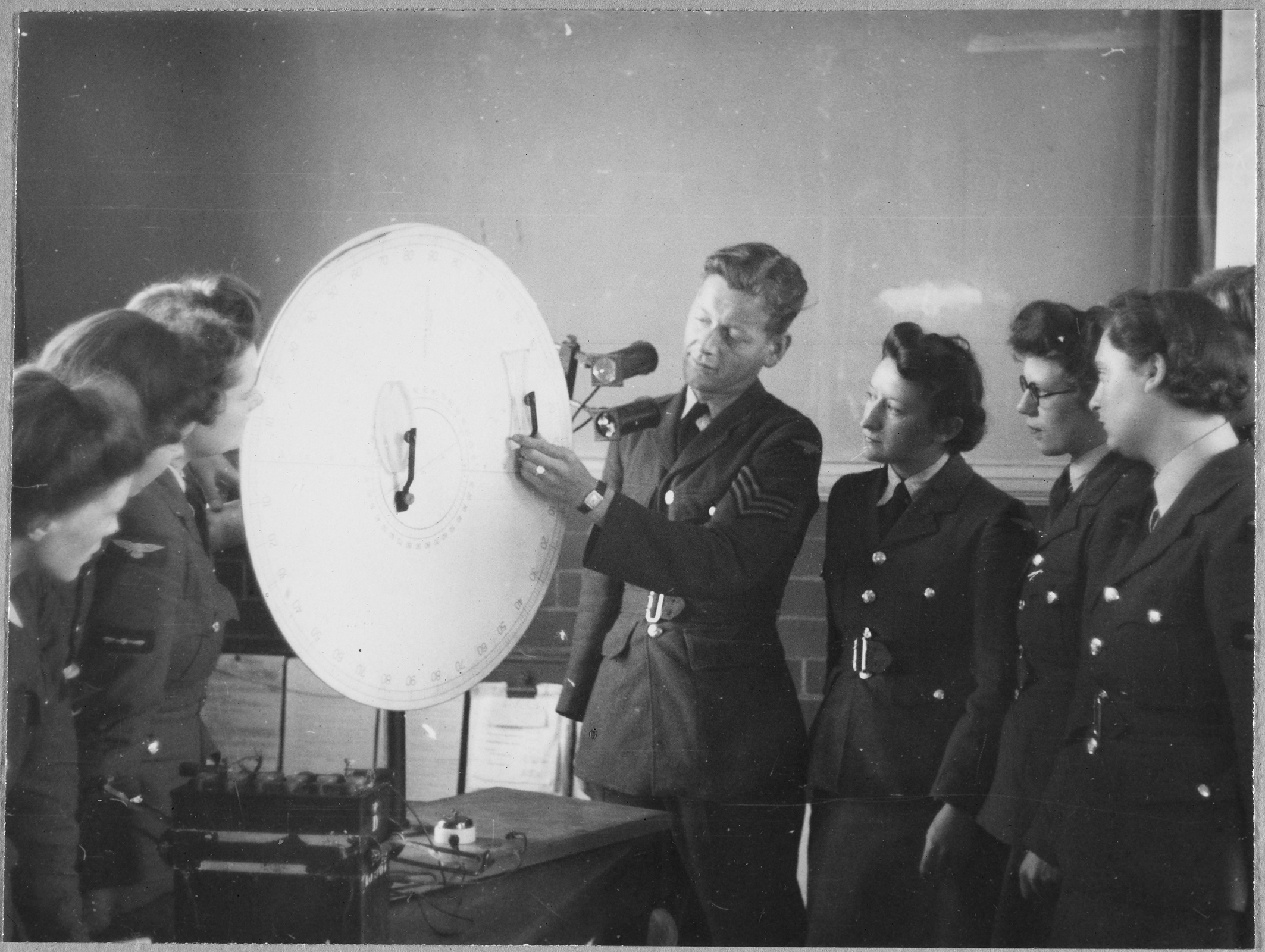 A group of Women's Auxiliary Air Force (WAAF) trainees observing an RAF Instructor demonstrating lens experiments on the optical disc, at the No.2 School of Photography in Blackpool