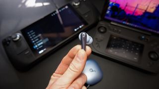 Soundcore Liberty 4 Pro earbuds on a black desk with various handheld gaming PCs.