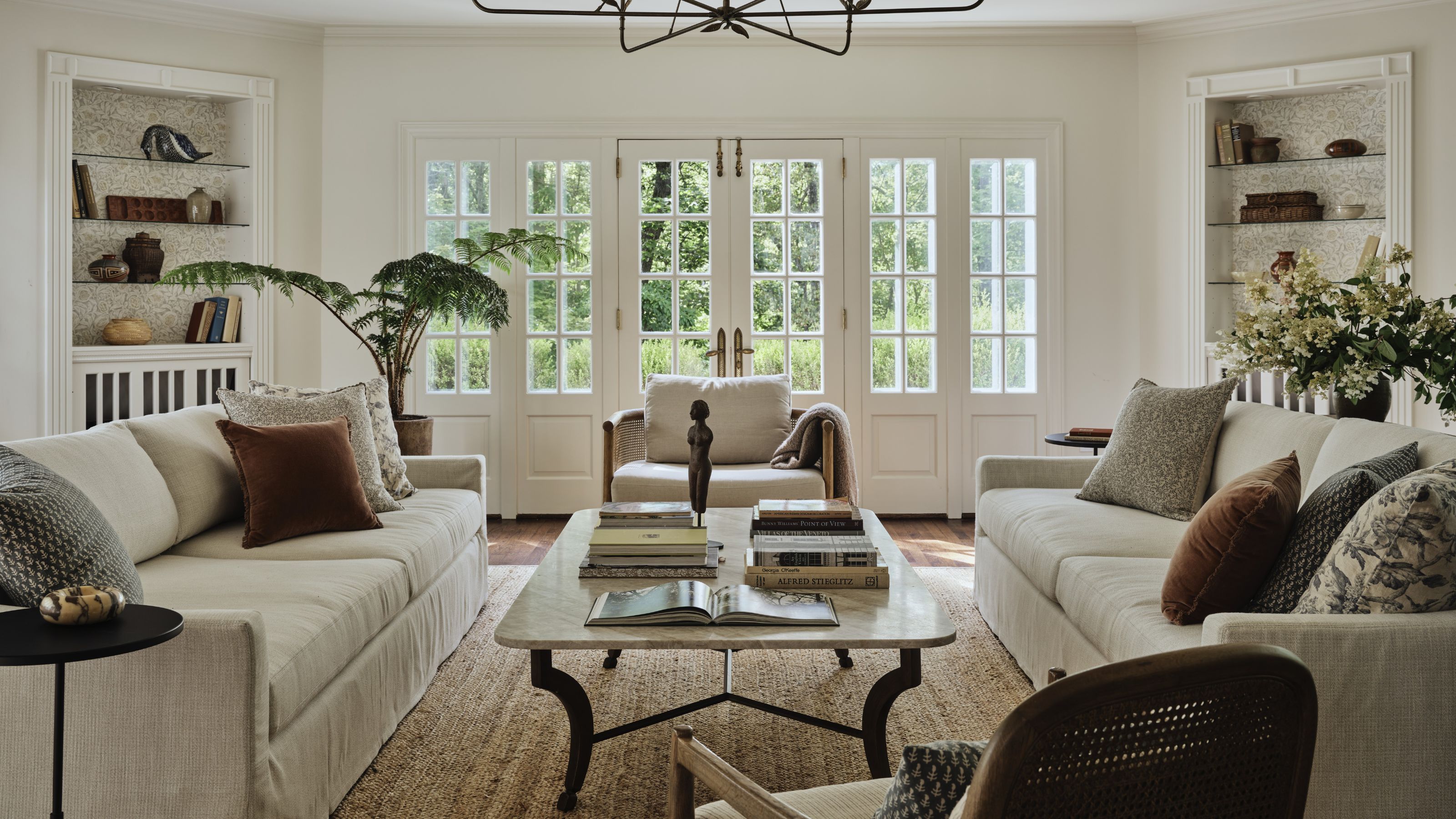 a white light filled Great Room with original bookcases, french doors, woven rug and two neutral linen couches