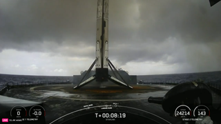 A new SpaceX Falcon 9 rockets sits on a drone ship landing pad in the Atlantic Ocean under gray clouds.