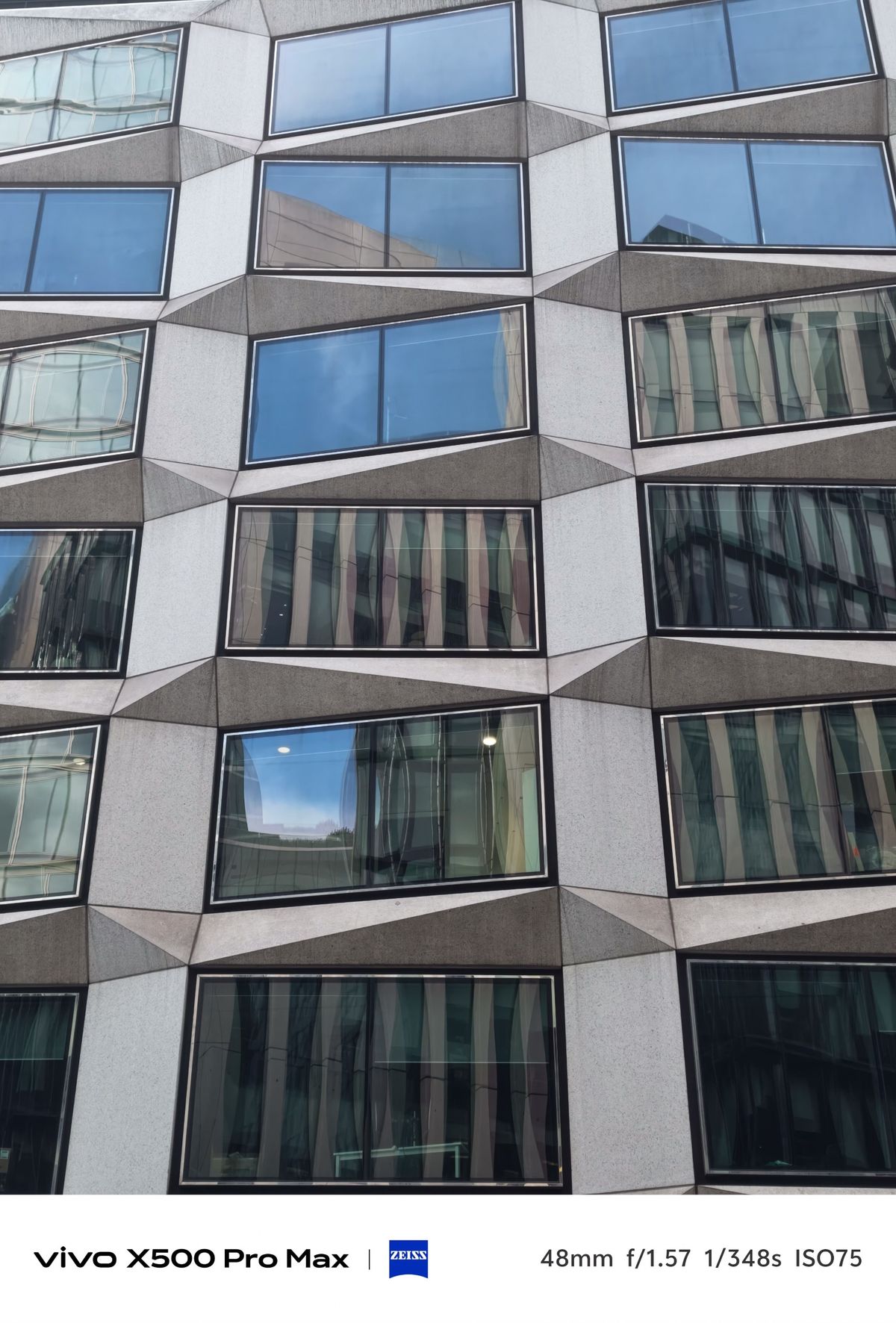 Close view of a modern geometric building facade with irregularly shaped windows reflecting the surrounding city.