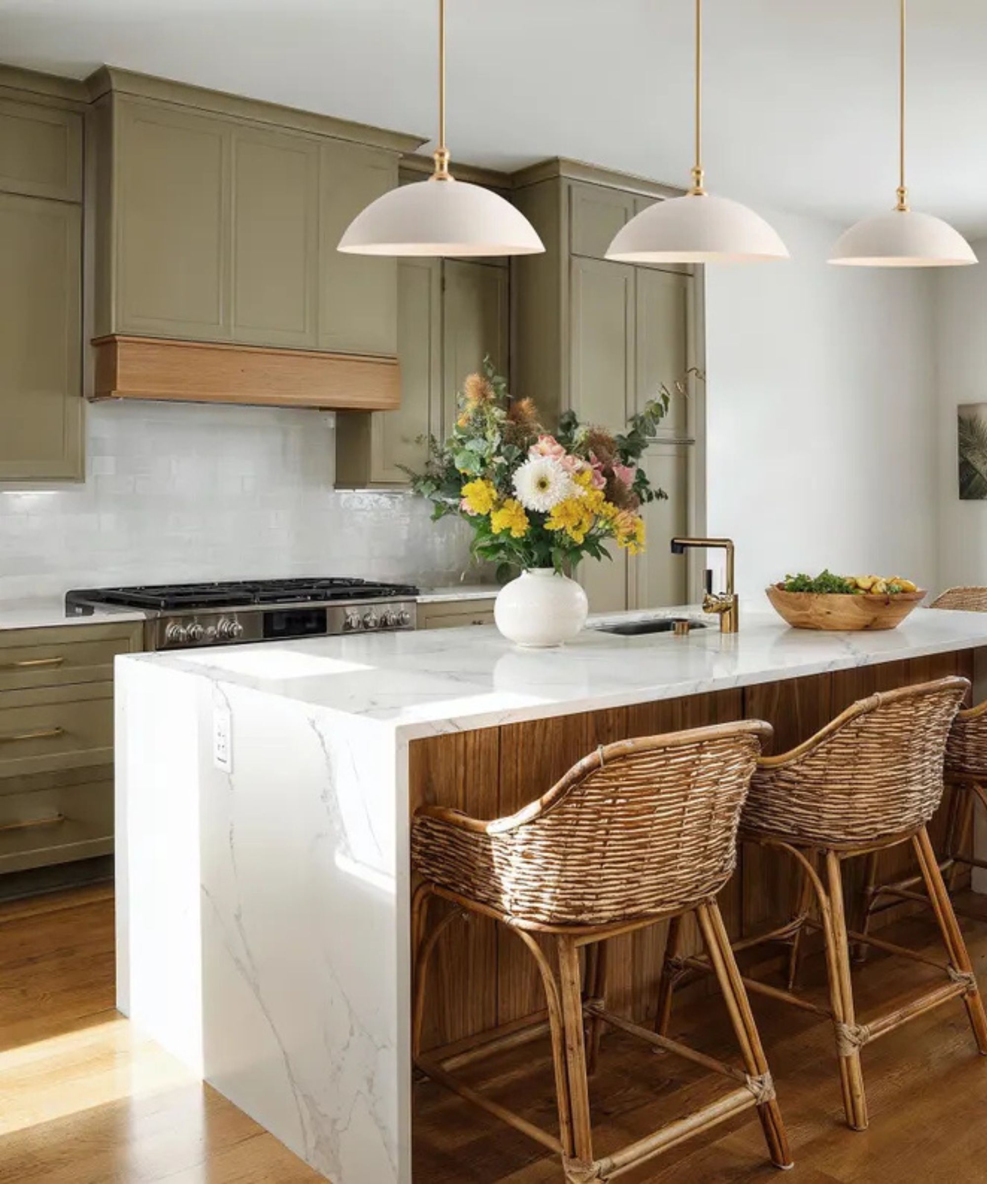 A white and green kitchen with a marble waterfall island countertops and white dome pendant lights
