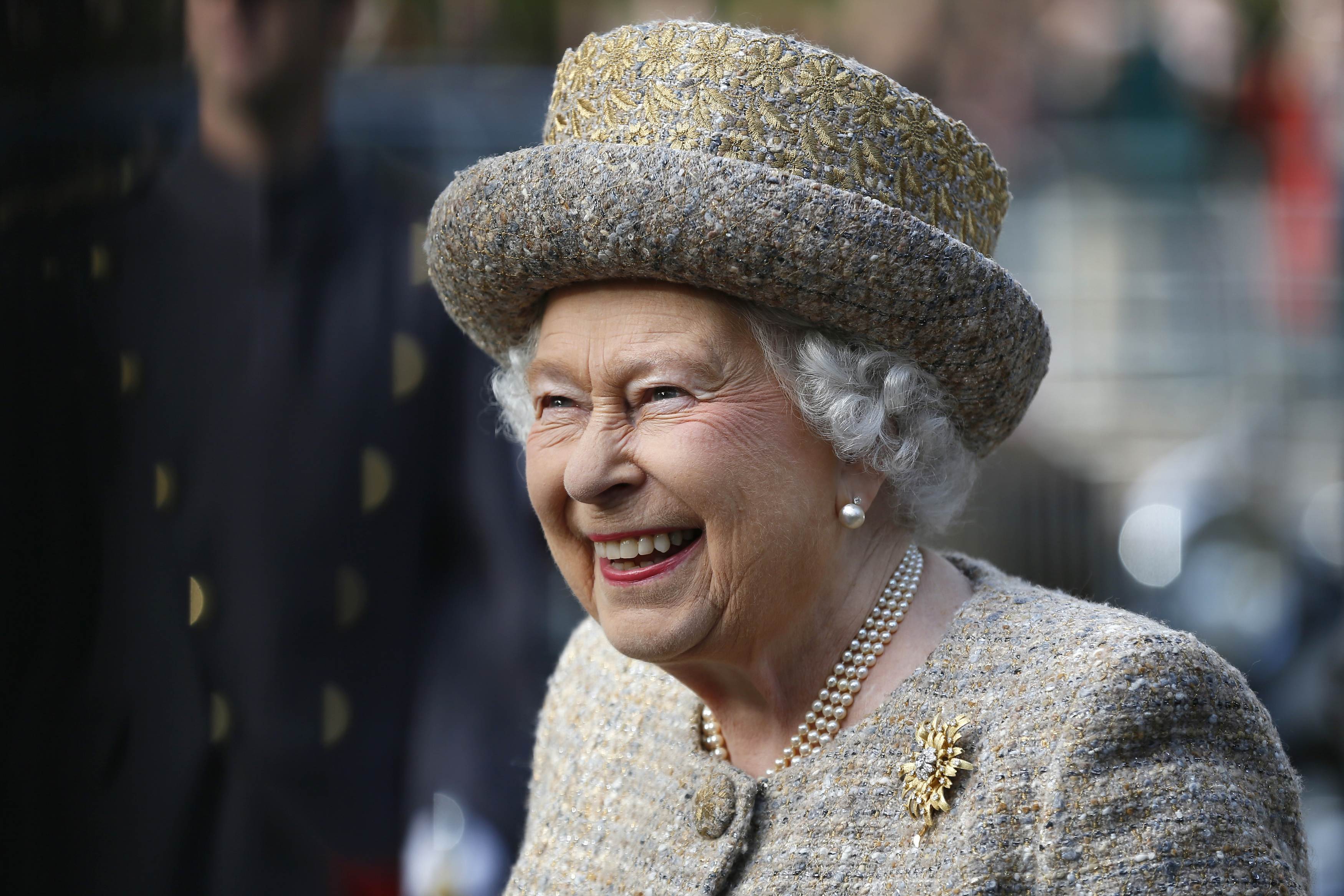 Queen Elizabeth wearing a gold hat and coat and laughing