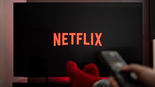 Mann mit Füßen auf einem Tisch, der Netflix im Fernsehen schaut