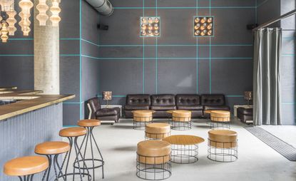 The Fantom bar with round chairs and tables and leather couches against a blue striped grey wall.