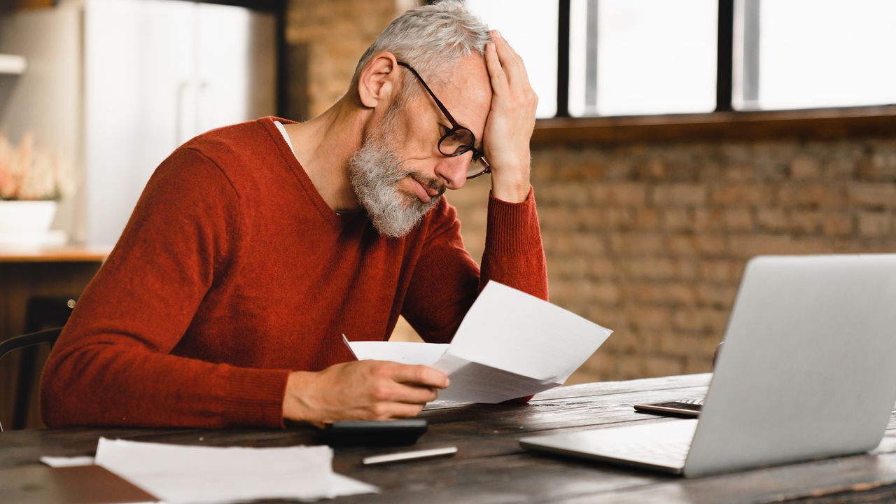 A male investor looks frustrated as he looks at paperwork, thinking he&#039;s made some common investing mistakes.