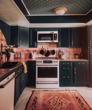 Dark green and blush kitchen, ceiling wallpapered in green art deco design, rug, brass fixtures and fittings