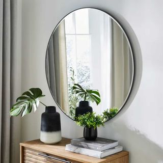 Neutral bedroom with a black frameless round mirror on the wall above a sideboard with plants
