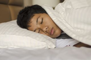 A close up teenage of a teenage by asleep lying on his side in bed
