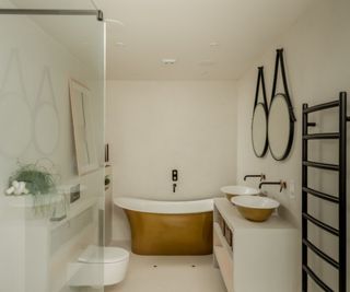 Neutral bathroom with a gold roll-top bathtub and a freestanding white bathroom vanity