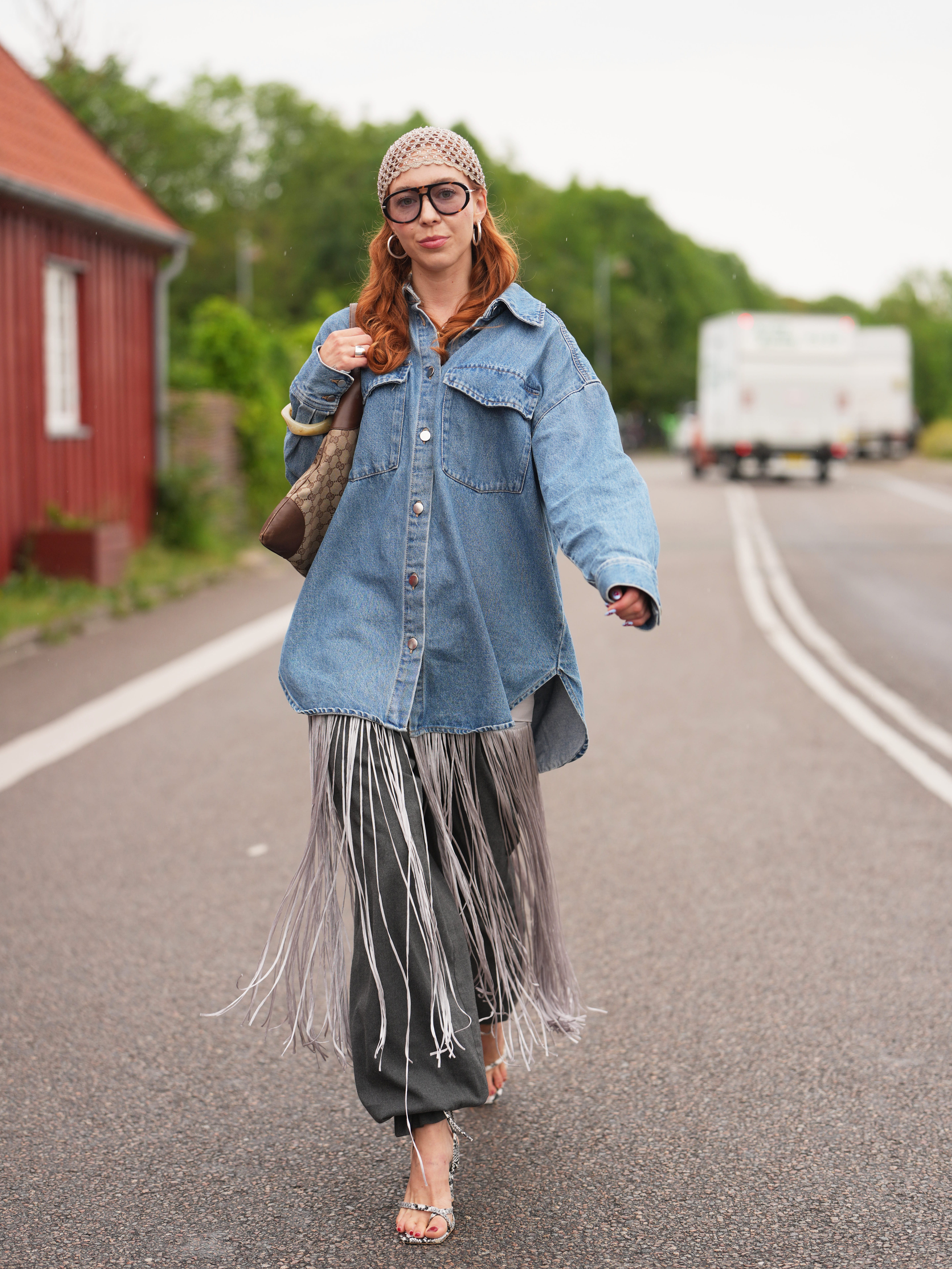 woman street style wearing a denim shirt and funky skirt with fun sunglasses and a headpiece