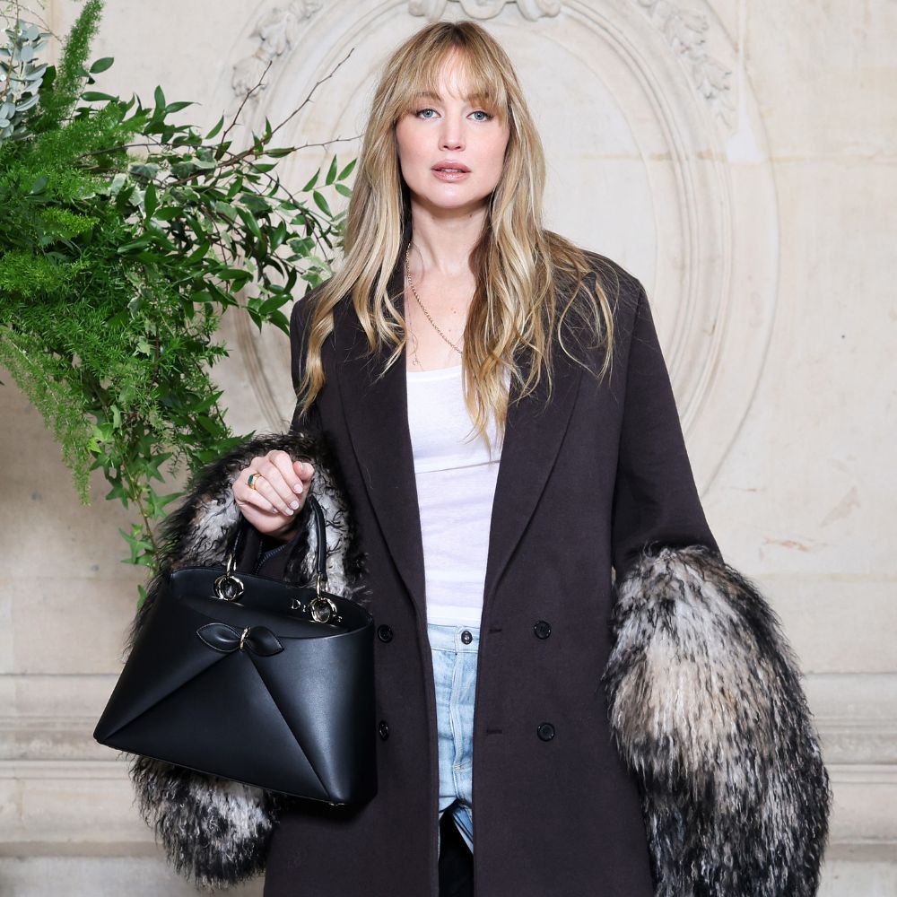 Jennifer Lawrence poses for a photo wearing puddle jeans with pointed-toe heels and a black tailored coat.