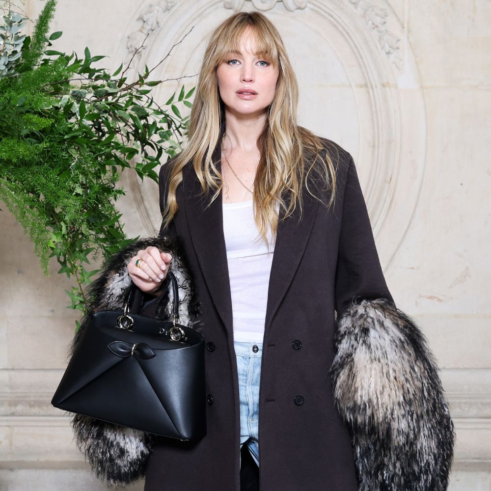 Jennifer Lawrence poses for a photo wearing puddle jeans with pointed-toe heels and a black tailored coat.