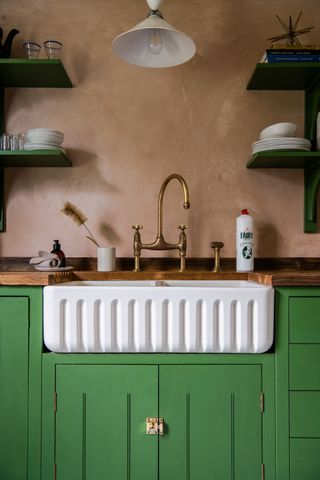 white scalloped sink in green kitchen with plaster pink walls