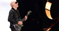 Joe Satriani wears dark shades and performs with his Ibanez "Chrome Boy" signature guitar.