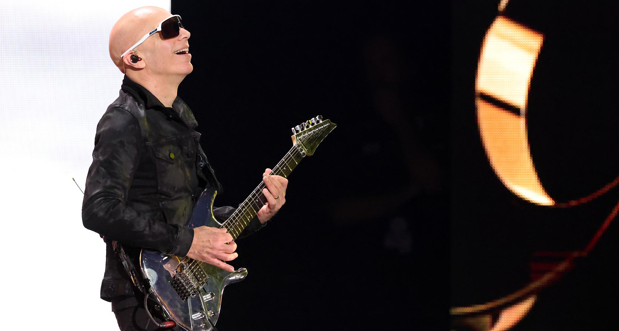 Joe Satriani wears dark shades and performs with his Ibanez "Chrome Boy" signature guitar.