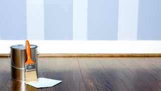 Can of paint and paint brush on wooden floor against painted striped wall