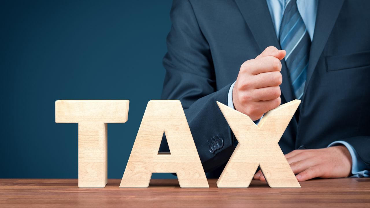 A man wearing a suit smashes his fist down on the X in the word tax. 