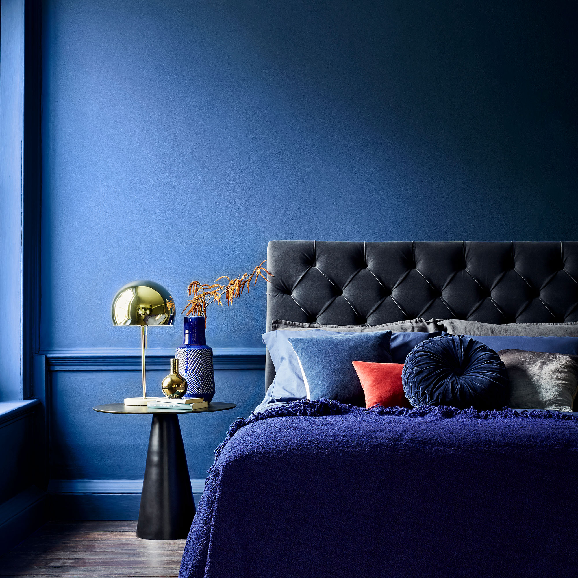 Bedroom with bright blue painted walls and velvet headboard