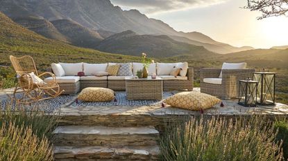 A rattan outdoor rocking chair on an outdoor patio area with a sectional sofa and a vista of mountains behind