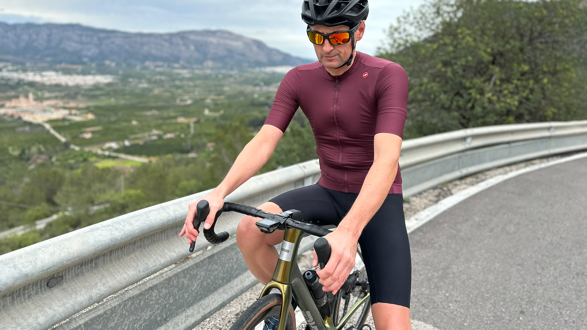 Man wearing a burgundy cycling jersey and black shorts sitting on a green bike