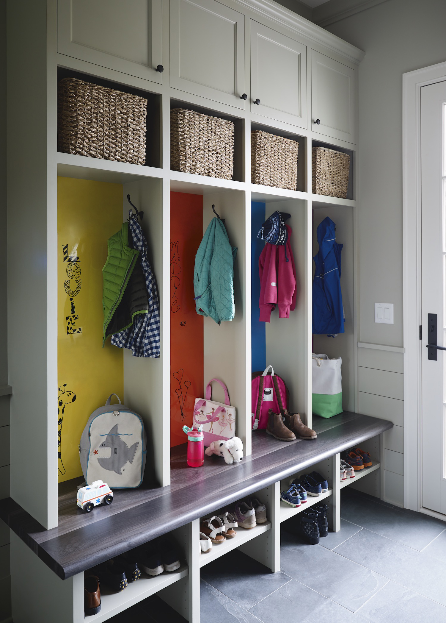 Floor to ceiling white mudroom storage unit filled with compartments of coats and bags