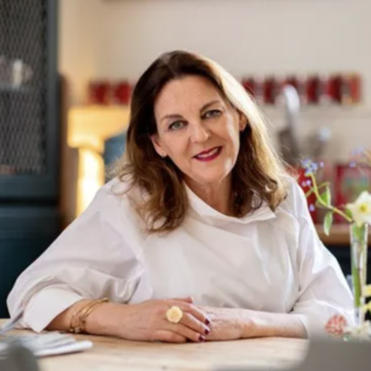A headshot of a woman with dark brown hair and a white blouse sat at a table and smiling at the camera
