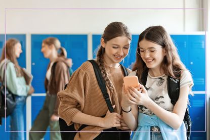 Two teenage girls laughing while looking at a mobile phone