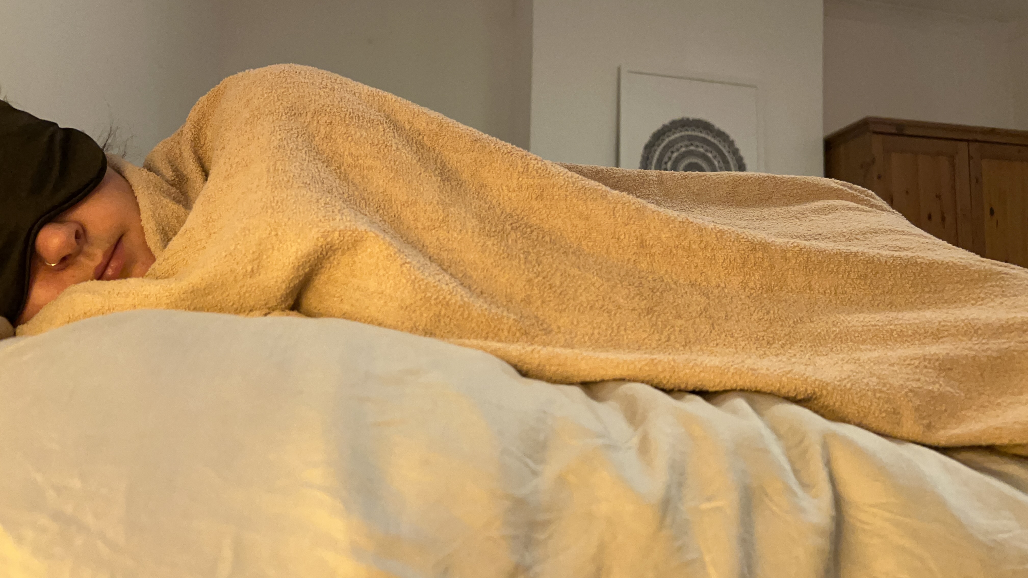 A woman lying on her side with a sleep mask on, wrapped in a pink towel