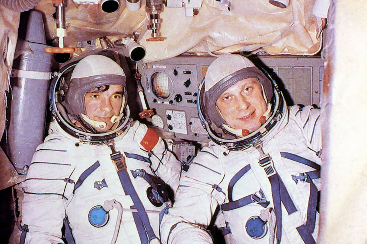 two men in white spacesuits inside a spacecraft