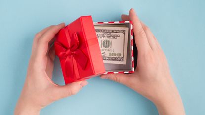 A woman opens a gift box of cash, only her hands showing.