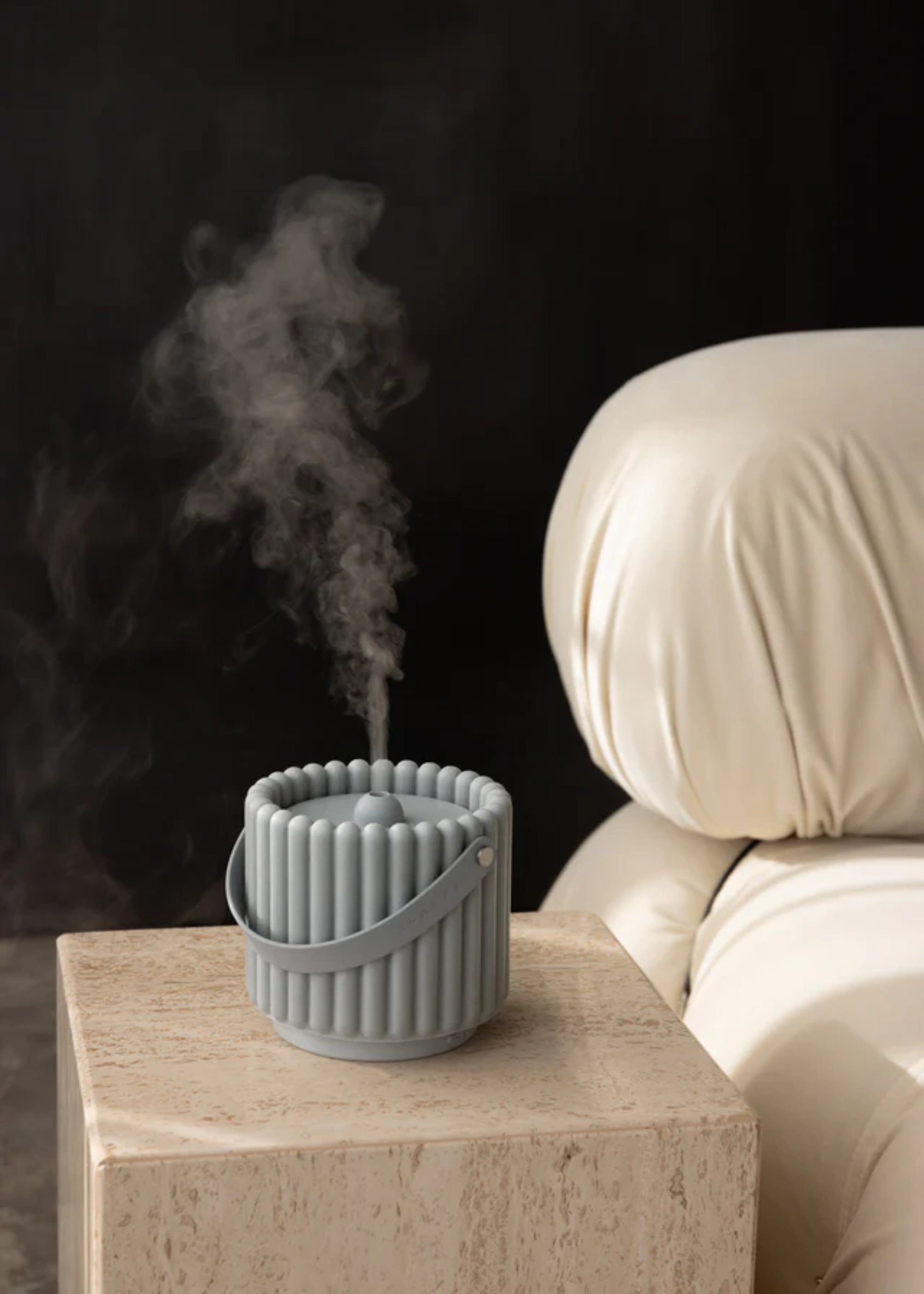 A travertine side table with a baby blue electronic diffuser by a white leather chair