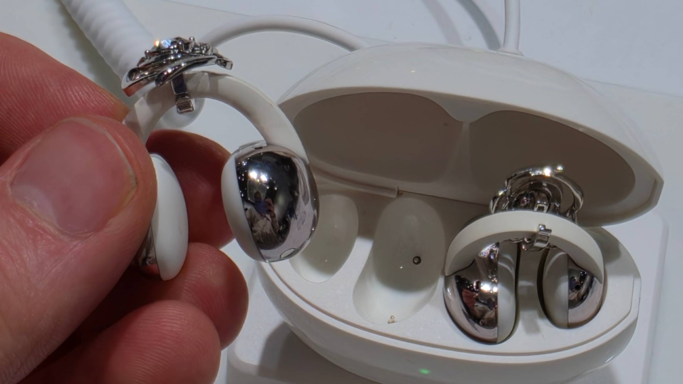 The TCL CrystalClip bud in a man's hand, with the case in the background.