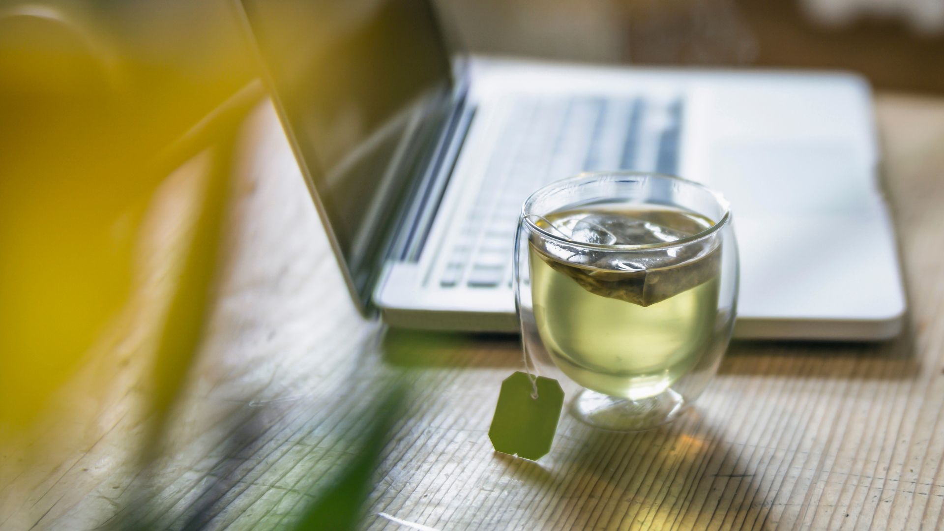 A glass cup of green tea on a table next to a laptop