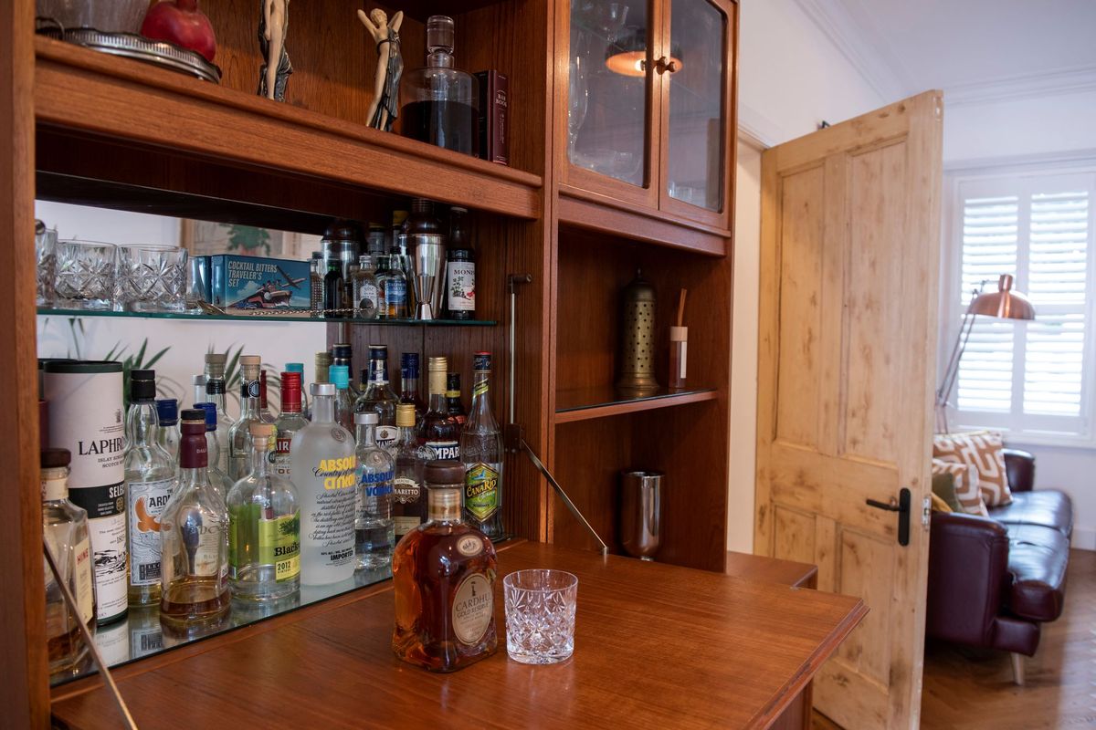 The living room features a drinks cabinet filled with numerous spirits with glasses stored above