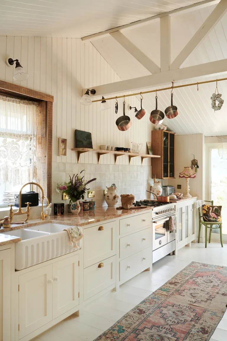 off white kitchen vintage style with shiplap walls, white painted floor, vintage rug, marble countertop, butler sink, tiled backsplash, open shelving, hanging utensils