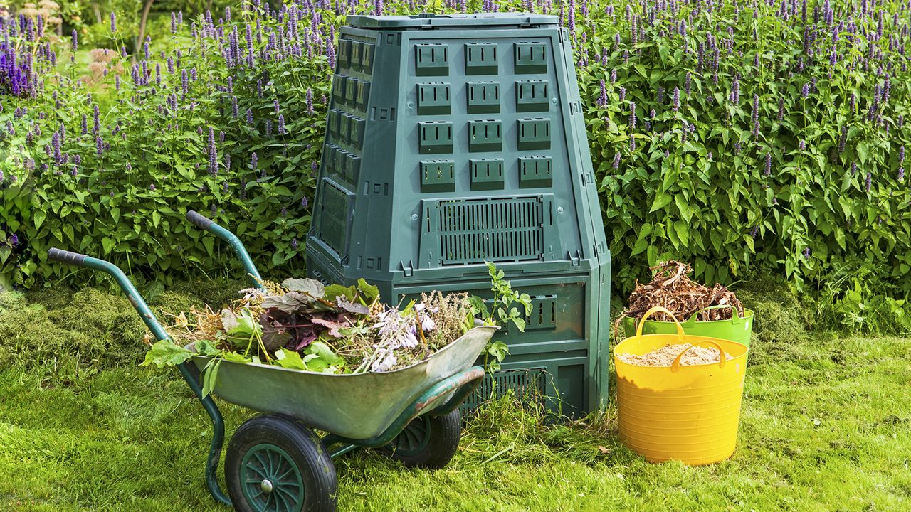 Home compost bin in the garden with wheelbarrow and buckets of composting ingredients