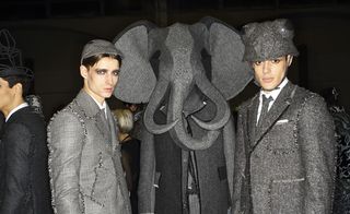 Two male models standing next to a grey elephant sculpture