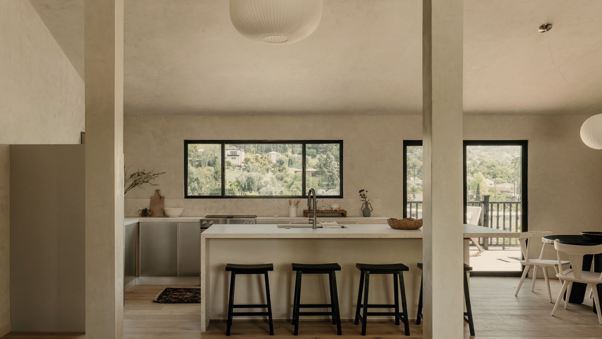 A Japanese-inspired minimalist kitchen and open dining space with paper lanterns, a white island, and black stools