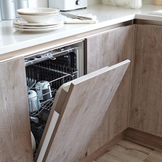 An open dishwasher in a natural wood-finish kitchen