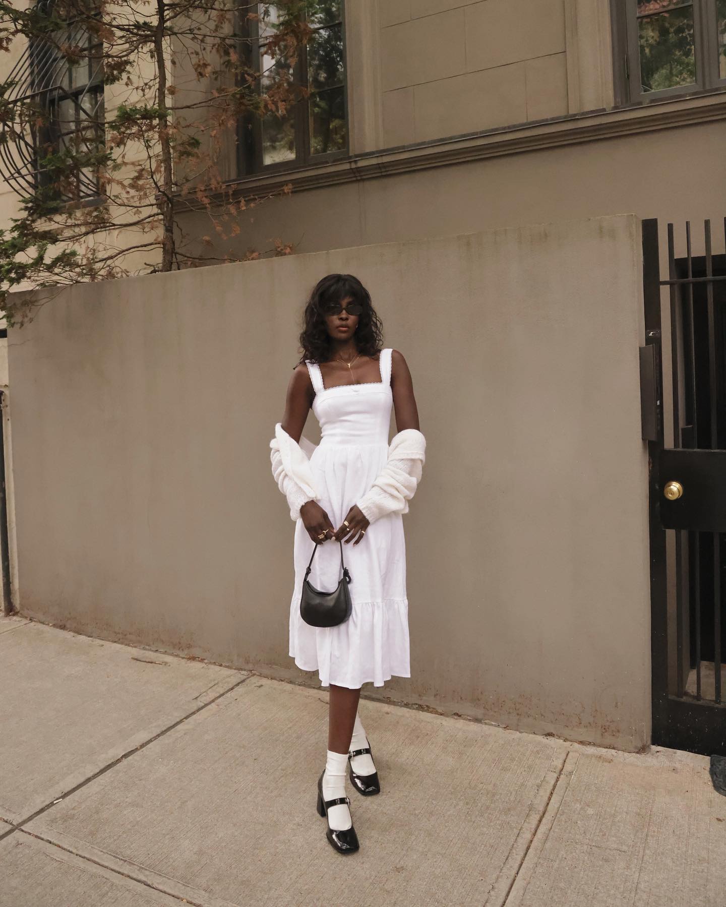 Woman on street wears white dress, white cardigan, white socks, black shoes