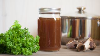 Bone broth in a mason jar with soup pot and beef bones in behind